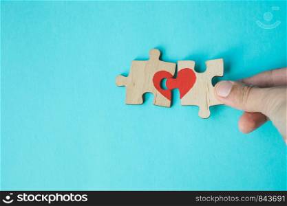Female hand connecting puzzle with drawn red heart on blue background. Love concept. St. Valentine day. Reconciliation. Reunion concept. Free space for text. Female hand connecting puzzle with drawn red heart on blue background. Love concept. St. Valentine day. Reconciliation. Reunion concept. Copy space.