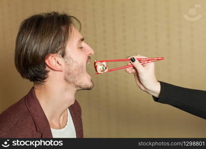 Female hand feeds the man with chopcticks. Japanese food