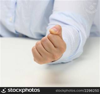 female hand folded into a fist on a white table. Strict leader, aggression and pressure on the person