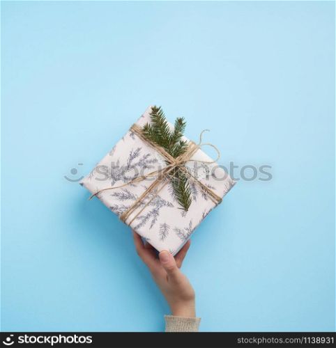 female hand hold a paper closed box on a blue background. Festive concept