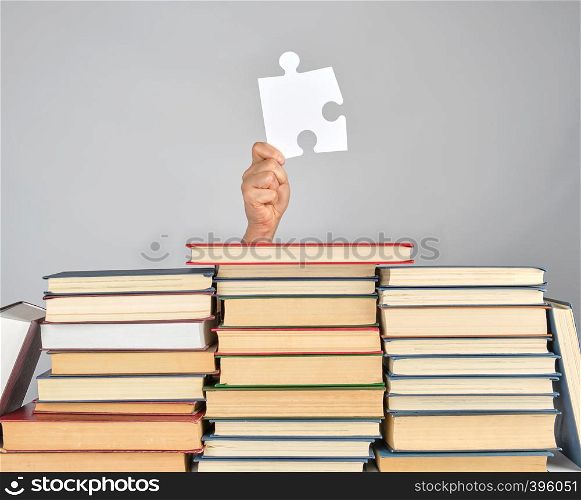 female hand holding a big white puzzle and a stack of books, gray background