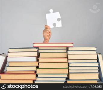female hand holding a big white puzzle and a stack of books, gray background