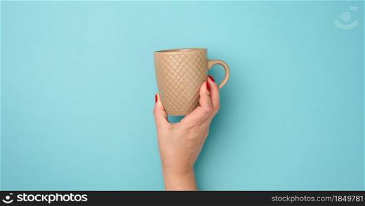 female hand holding a brown ceramic mug on a blue background, break time and drink coffee, banner