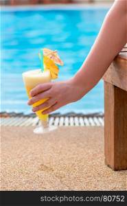 female hand holding a cocktail, picture on the background of the pool