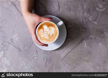 Female hand holding a cup of cappuccino with figure cream. Top view with copy space. Cup of cappuccino with figure cream