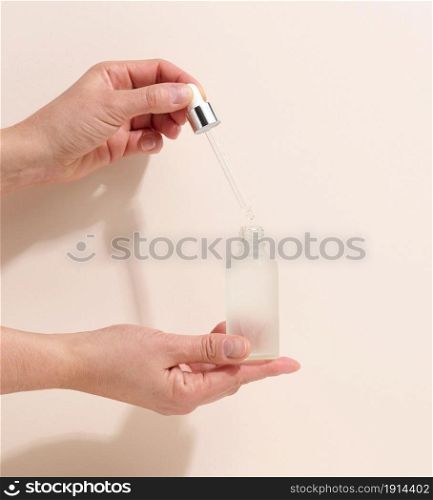 female hand holding a glass bottle and dropper for cosmetics on a beige background