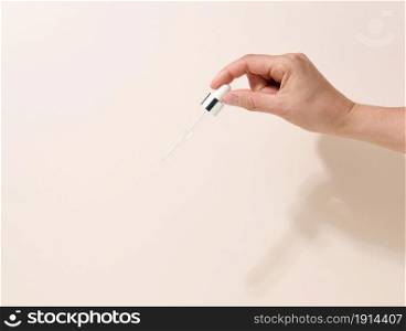 female hand holding a glass dropper for cosmetics on a beige background
