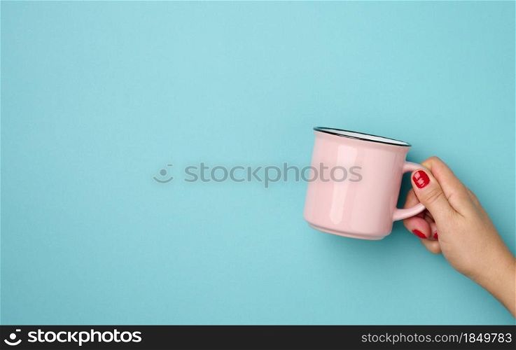 female hand holding a pink ceramic mug on a blue background, break time and drink coffee, copy space