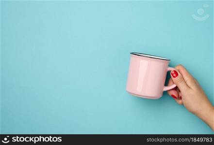female hand holding a pink ceramic mug on a blue background, break time and drink coffee, copy space