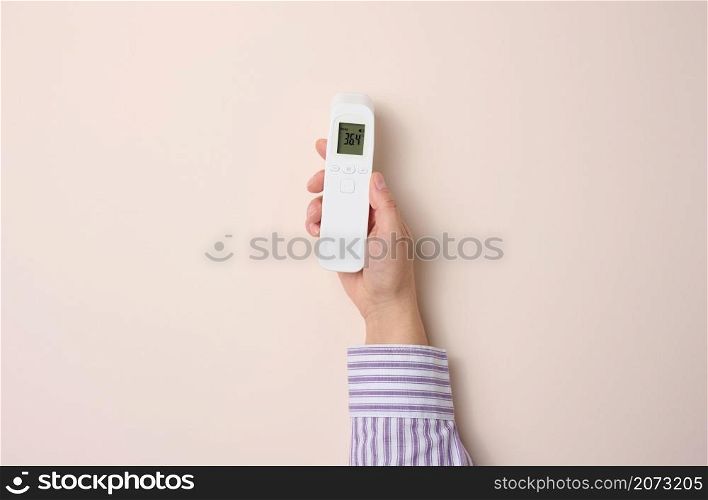 female hand holding a plastic non-contact thermometer on a beige background