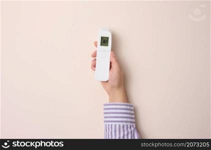 female hand holding a plastic non-contact thermometer on a beige background