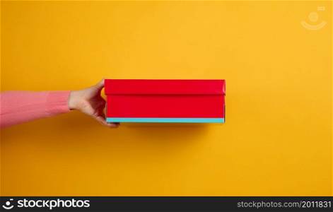 female hand holding a red cardboard box on a yellow background, delivery