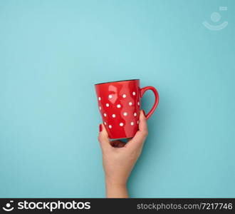 female hand holding a red ceramic mug on a blue background, break time and drink coffee