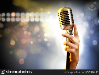 Female hand holding a single retro microphone against colourful background