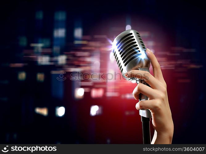 Female hand holding a single retro microphone against colourful background