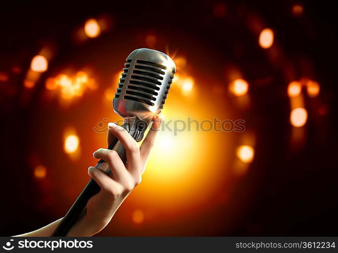 Female hand holding a single retro microphone against colourful background