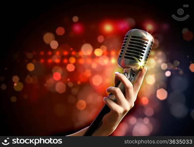 Female hand holding a single retro microphone against colourful background