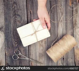 female hand holding a stack of cards tied with a brown rope over a gray wooden table