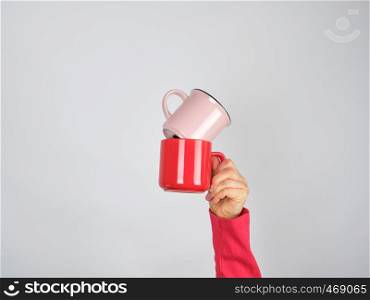 female hand holding a stack of ceramic mugs, gray background