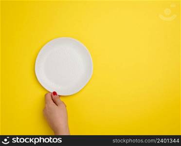 female hand holding a white empty round plate on a yellow background, top view, copy space