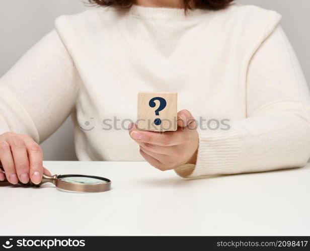 female hand holding a wooden cube with a question mark, concept of answers and questions, suspense and solution methods
