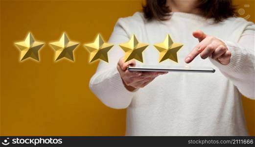 female hand holding an electronic gadget tablet on a yellow background, five gold stars. Business evaluation concept by users, rating and voting