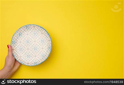 female hand holding an empty round plate on a yellow background, top view