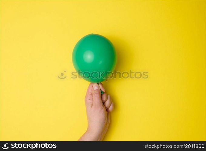female hand holding an inflated green air balloon on a yellow background, close up