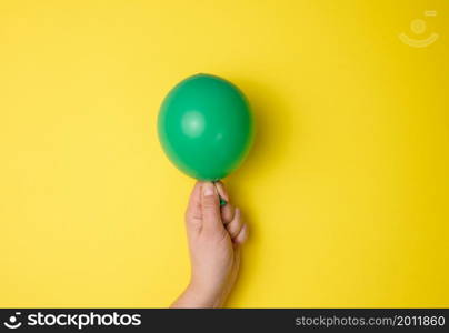 female hand holding an inflated green air balloon on a yellow background, close up