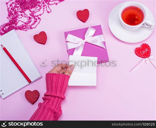 female hand holding blank white paper business cards over a table with a cup of tea, top view