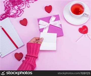 female hand holding blank white paper business cards over a table with a cup of tea, top view