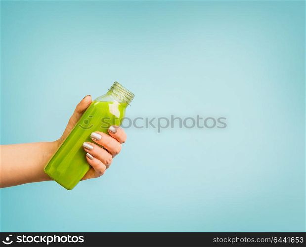 Female hand holding bottle with green summer beverage: smoothie or juice at blue background.