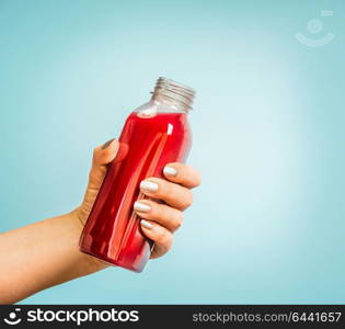 Female hand holding bottle with red summer drink: smoothie or juice at blue background.