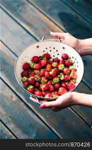 Female hand holding bowl of fresh strawberries sprinkled raindrops over wooden table