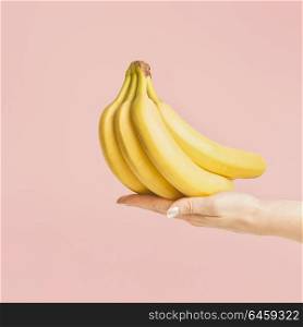 Female hand holding bunch of bananas at pastel pink background, front view