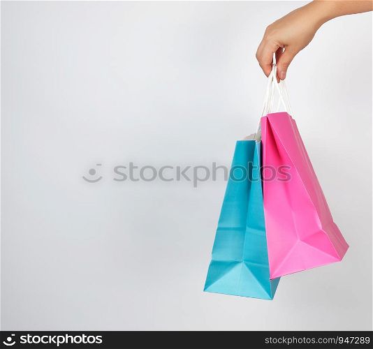 female hand holding colored paper shopping packaging bags on white background, concept of seasonal sales