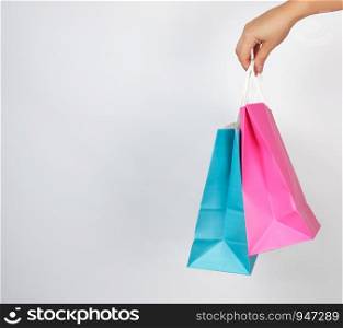 female hand holding colored paper shopping packaging bags on white background, concept of seasonal sales