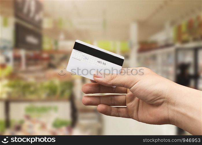 female hand holding credit card with blurry supermarket background