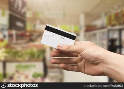 female hand holding credit card with blurry supermarket background