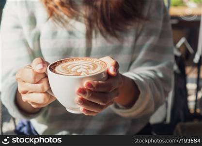 female hand holding cup of hot cocoa or chocolate on wooden table, close up
