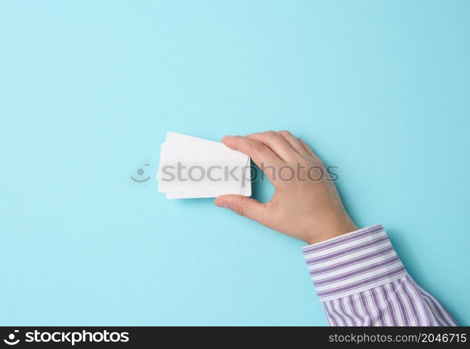 Female hand holding empty paper white business card on a blue background. Copy space