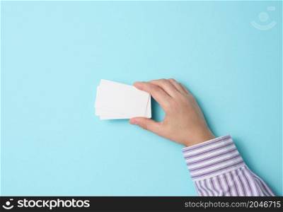Female hand holding empty paper white business card on a blue background. Copy space