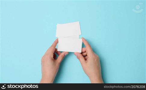Female hand holding empty paper white business card on a blue background. Copy space