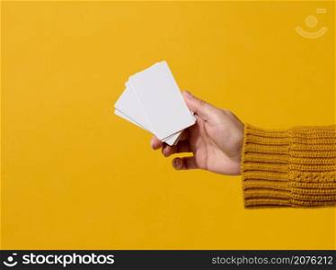 Female hand holding empty paper white business card on a yellow background. Copy space