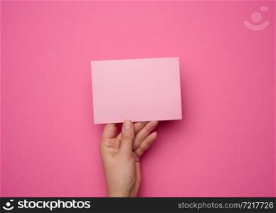 Female hand holding empty pink paper on a pink background. Copy paste image or text, close up
