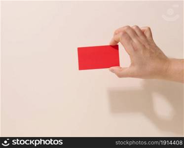 Female hand holding empty red paper on a beige background. Copy paste image or text, close up