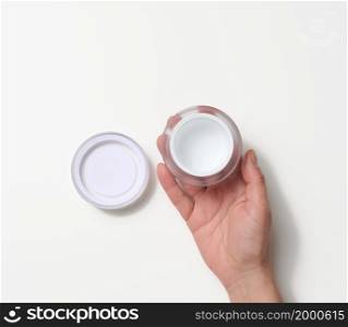 female hand holding empty white plastic jar. Packaging for cream, gel, serum, advertising and product promotion