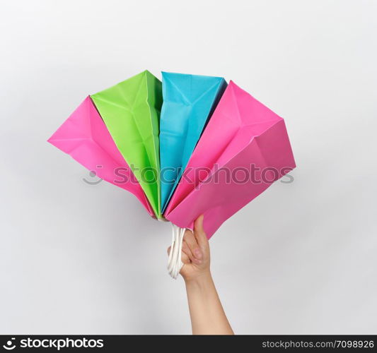 female hand holding four colored paper shopping packaging bags on white background, concept of seasonal sales