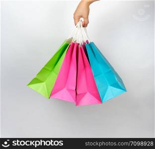 female hand holding four colored paper shopping packaging bags on white background, concept of seasonal sales