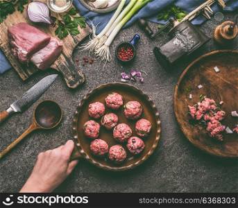 Female hand holding frying pan with meat balls on kitchen table with ingredients and tools, top view